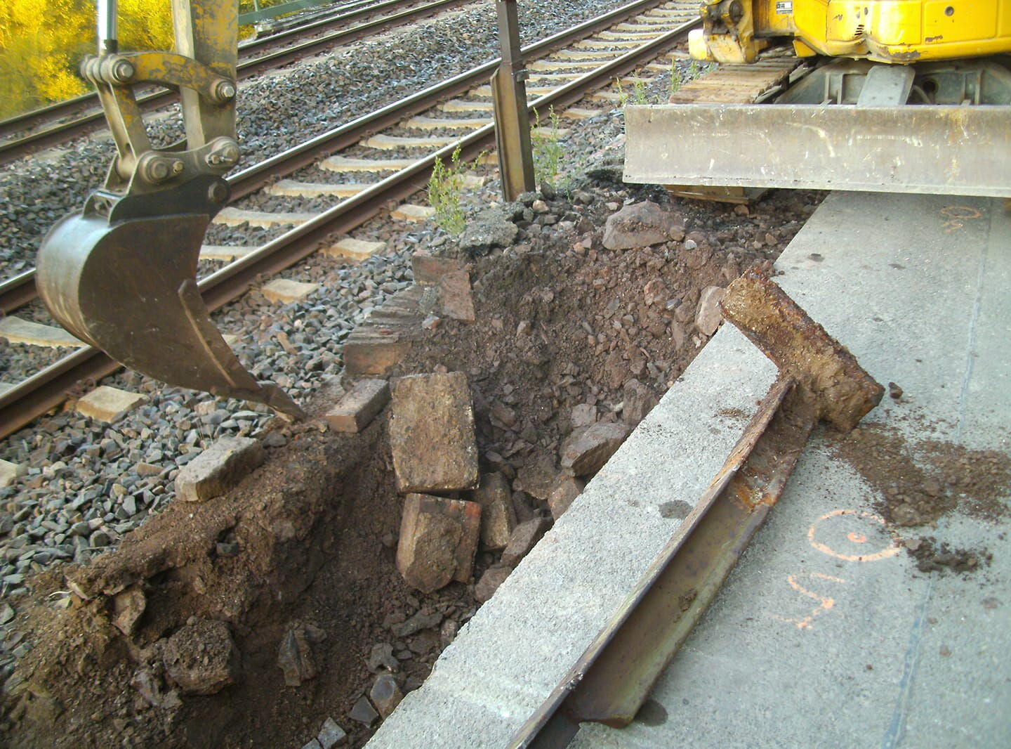 Neben den Bahngleisen, hebt ein Bagger ein Loch aus.