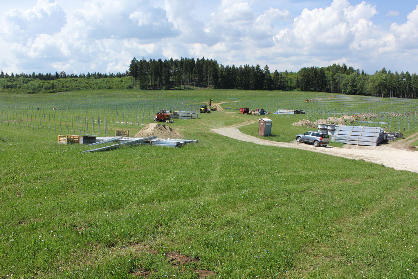 Eine Grüne Wiese mit dem Aufbau einer Photovoltaikanlage.